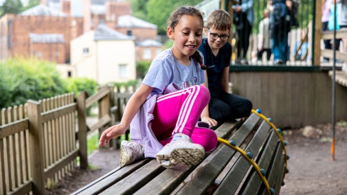Smiling children sat on a tube like play structure